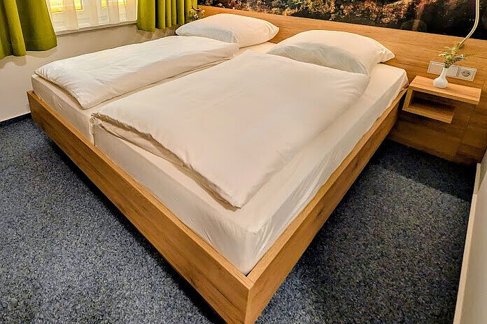 Akademiehotel Jena – Doppelzimmer 2025 Modern eingerichtetes Doppelzimmer im Akademiehotel mit großem Bett, Holzrahmen, Wandbild mit Landschaftspanorama und Fenster mit grünen Vorhängen